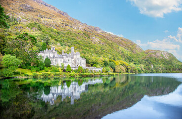 Fototapeta premium The James Franklin Fuller-designed Kylemore Abbey, a Benedictine Monastery in Connemara, County Galway, Ireland and its surrounding tree-covered mountains reflect in the water on a summer day.