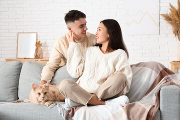 Beautiful young couple with cute Maine Coon cat on sofa in living room