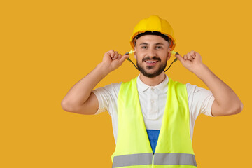 Male builder putting earplugs on yellow background