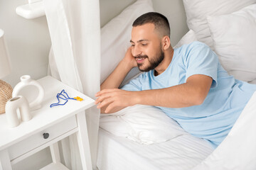 Young man taking earplugs from table in bedroom