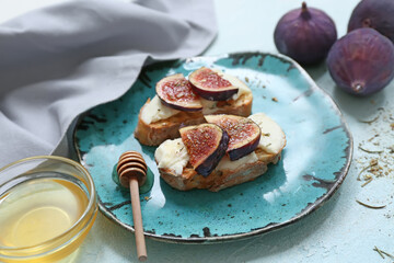 Plate of delicious fig bruschetta with ricotta cheese and bowl of honey on light blue background, closeup