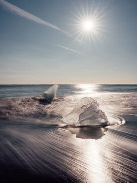 Long exposure image of broken off glacier ice washed up on shore of black sand Diamond Beach on Iceland