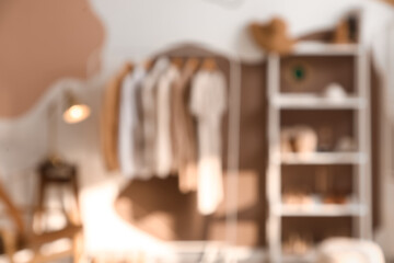 Rack with clothes, shelving unit and lamp on stool near colorful wall in dressing room. Blurred view