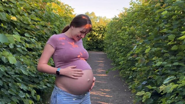 beautiful pregnant young woman walking in park in warm summer weather enjoying third trimester in green labyrinth