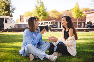Two women friends sisters sitting in the park and have emotional talk conversation sitting in the...
