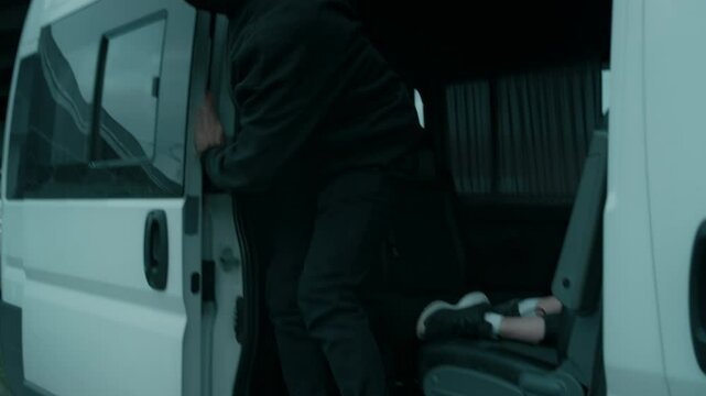 Side shot of anonymous male maniac in mask dragging unconscious female victim into van, looking around and shutting door, kidnapping girl in city