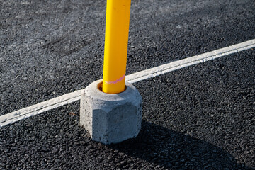 Yellow pipe on a light pole base on asphalt.