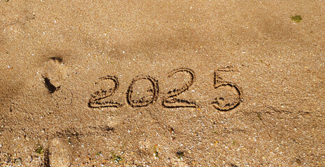 2025 written on the sea sand. Sandy textured background. Concept of celebrating New Year on a tourist trip. Template for greeting card, postcard, invitation, promotion materials, websites