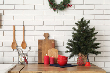 Small Christmas tree with burning candles and utensils on counter near white brick wall in kitchen