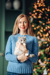 Obraz premium A beautiful woman at home near the Christmas tree with her beloved pet cat