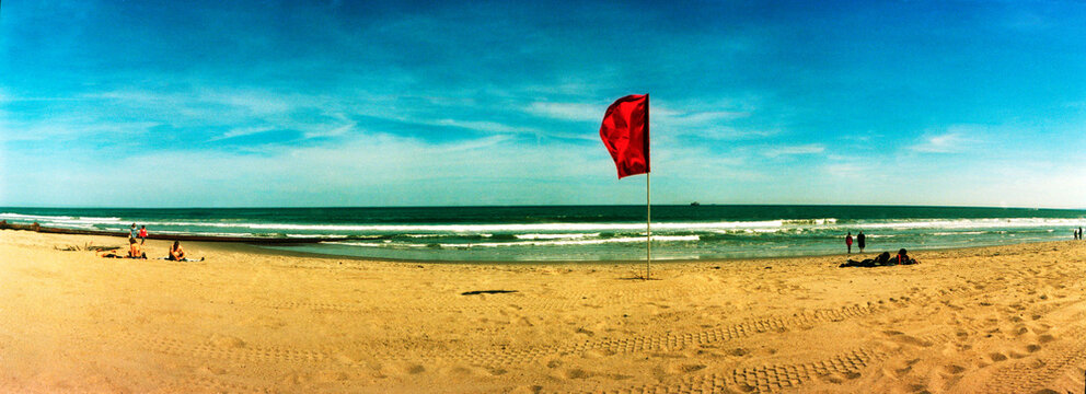 Panoramic image of a red flag waving on Coney Island beach. 