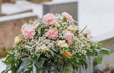 Frozen memorial flowers on the grave on a frosty day in January. The funeral flowers have frost. Frozen pink carnations on the grave.