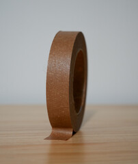 A roll of brown craft tape lies on a wooden surface.