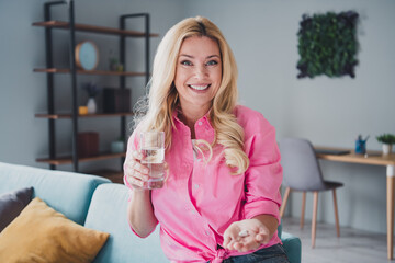 Young woman relaxing at home in living room, smiling while holding glass of water, enjoying leisure time
