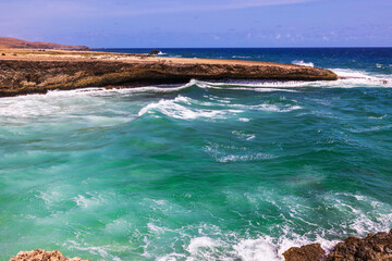Waves crashing against rocky coastline with turquoise water Caribbean sea in Arikok National Park, Aruba.