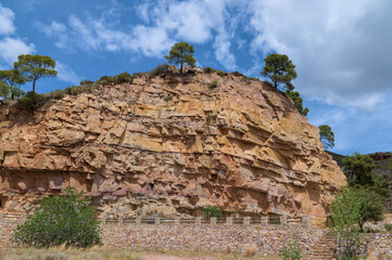 Rugged rock cliff with layers of exposed stone under a bright blue sky.