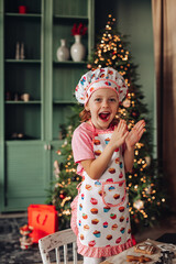 a girl child in the kitchen with a Christmas tree is preparing or cooking ginger cookies for Christmas or New year