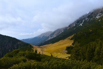 View of Dolga Njiva alpine pasture under cloud covered mountain range in Karavanke mountains in Gorenjska, Slovenia