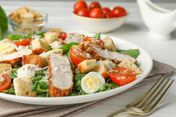 Tasty Caesar salad with chicken and tomatoes on white wooden table, closeup
