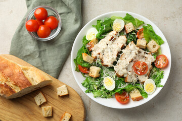 Tasty Caesar salad with chicken, bread and tomatoes in bowl on gray textured table, flat lay