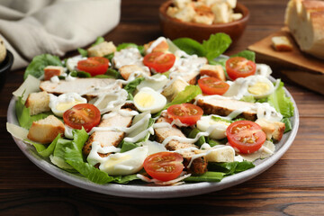 Delicious Caesar salad with chicken on wooden table, closeup