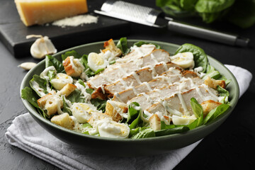 Delicious Caesar salad with chicken on black textured table, closeup