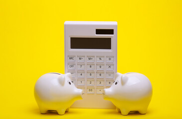 Ceramic white piggy banks with calculator on a yellow background. Business concept. Conceptual photo