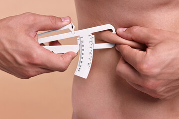 Man measuring body fat with caliper on beige background, closeup
