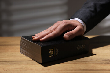 Man taking oath with his hand on Bible at wooden table, closeup