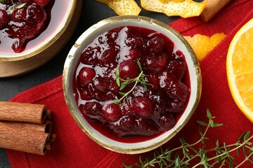 Tasty cranberry sauce in bowls, orange peels, thyme and cinnamon on table, top view