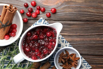 Tasty cranberry sauce in gravy boat, berries and spices on wooden table, flat lay. Space for text