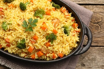 Tasty rice with vegetables in baking dish on wooden table, top view