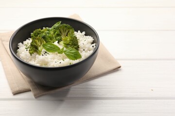 Tasty rice with broccoli and basil in bowl on white wooden table, closeup. Space for text