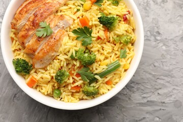Tasty rice with vegetables and chicken on grey table, top view