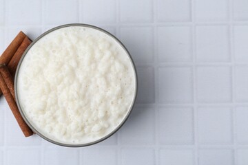 Delicious rice pudding with cinnamon sticks on white tiled table, top view. Space for text