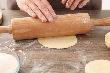 Making pirozhki (stuffed pastry pies). Woman shaping dough with rolling pin at wooden table, closeup