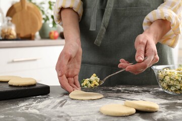 Woman making pirozhki (stuffed pastry pies) with eggs and dill at gray table indoors, closeup