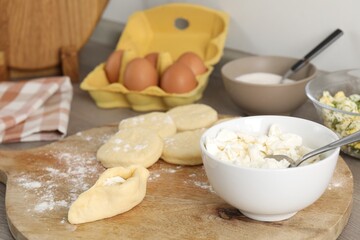 Making pirozhki (stuffed pastry pies). Pieces of dough with cottage cheese on table, closeup