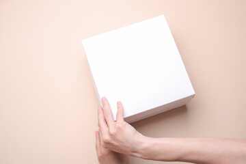 Obraz premium Female hands open white cardboard box on beige background. Mockup for design. Top view
