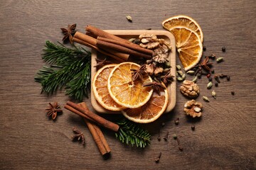 Different spices, dried orange slices and fir tree branches on wooden table, flat lay. Christmas season