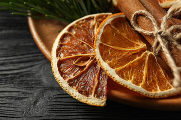 Different spices, dried orange slices and fir tree branches on black wooden table, closeup. Christmas season