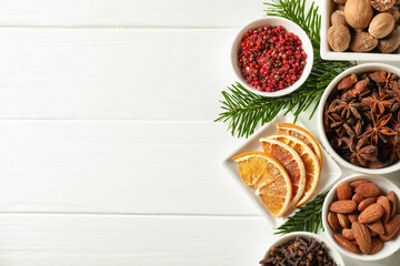 Different spices, dried orange slices and fir tree branches on white wooden table, flat lay with space for text. Christmas season