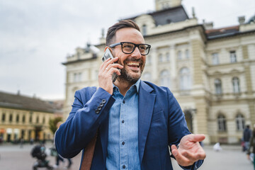 cheerful adult businessman go from work and talk on mobile phone