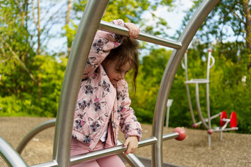 Little girl with long hair climbing on playground in summer. Healthy active mischievous child...