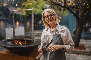 portrait of woman waitress hold kitchen tongs and stand behind grill