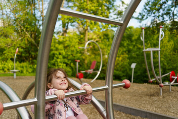 Obraz premium Little girl with long hair climbing on playground in summer. Healthy active mischievous child concept