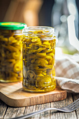 Pickled sliced jalapeno peppers in jar on wooden table.
