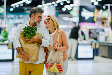 Happy senior couple carrying grocery bags while walking through supermarket