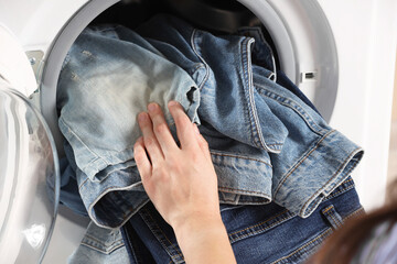 Woman putting dirty jeans and other denim clothes into washing machine, closeup
