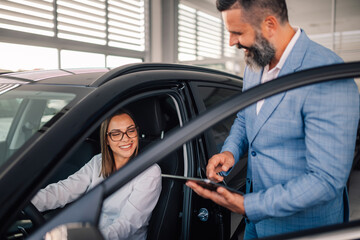 Woman in car receiving keys from man in blue suit, smiling.